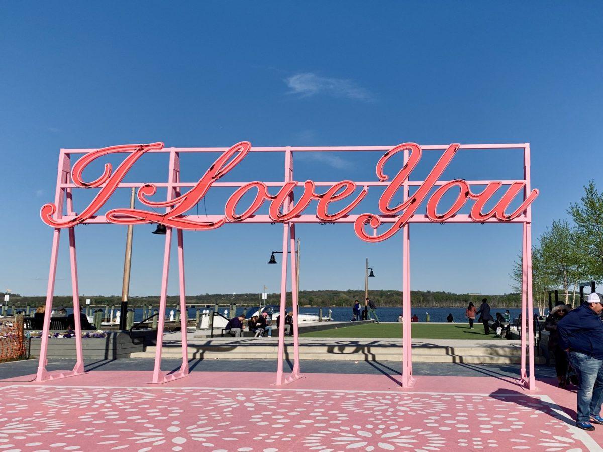 A+pink%2C+cursive+I+Love+You+sign+sits+in+front+of+the+blue+sky.+It+is+clear+day+on+the+Old+Town+Waterfront%2C+and+the+rotating+art+installation+is+occupied.