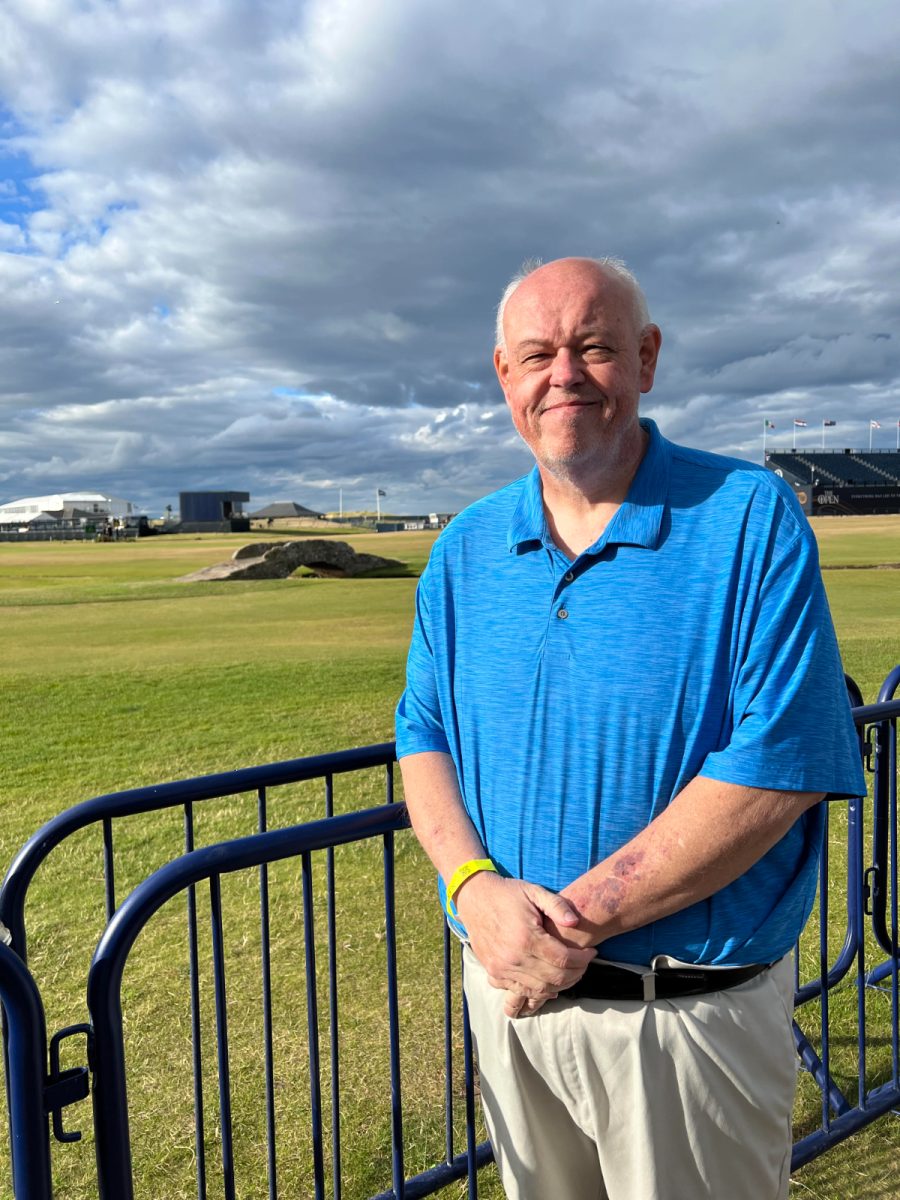 Kevin Burkhead posing in front of a golf course at the 150th Open Championship in St. Andrews, Scotland