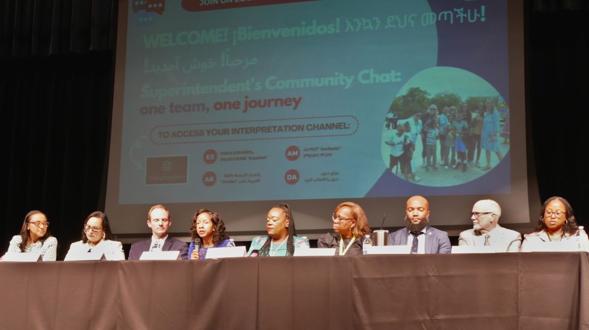 From left: Superintendent Melanie Kay-Wyatt, Chief of School and Community Relations Julia Burgos, Chief Accountability and Research Officer Clinton Page, Chief Operating Officer Alicia Hart, Chief Academic Officer Pierrette Finney, Chief of Student Services and Equity Marcia Jackson, Chief Financial Officer Dominic Turner, Acting Executive Director of Human Resources Rene Paschal and Executive Director of Human Resources Kamika Valmond sit on a panel in the ACPS auditorium. Behind them is a graphic that says “Welcome!” in English, Spanish, Amharic, Dari and Arabic. Interpretation channel access links are listed below.