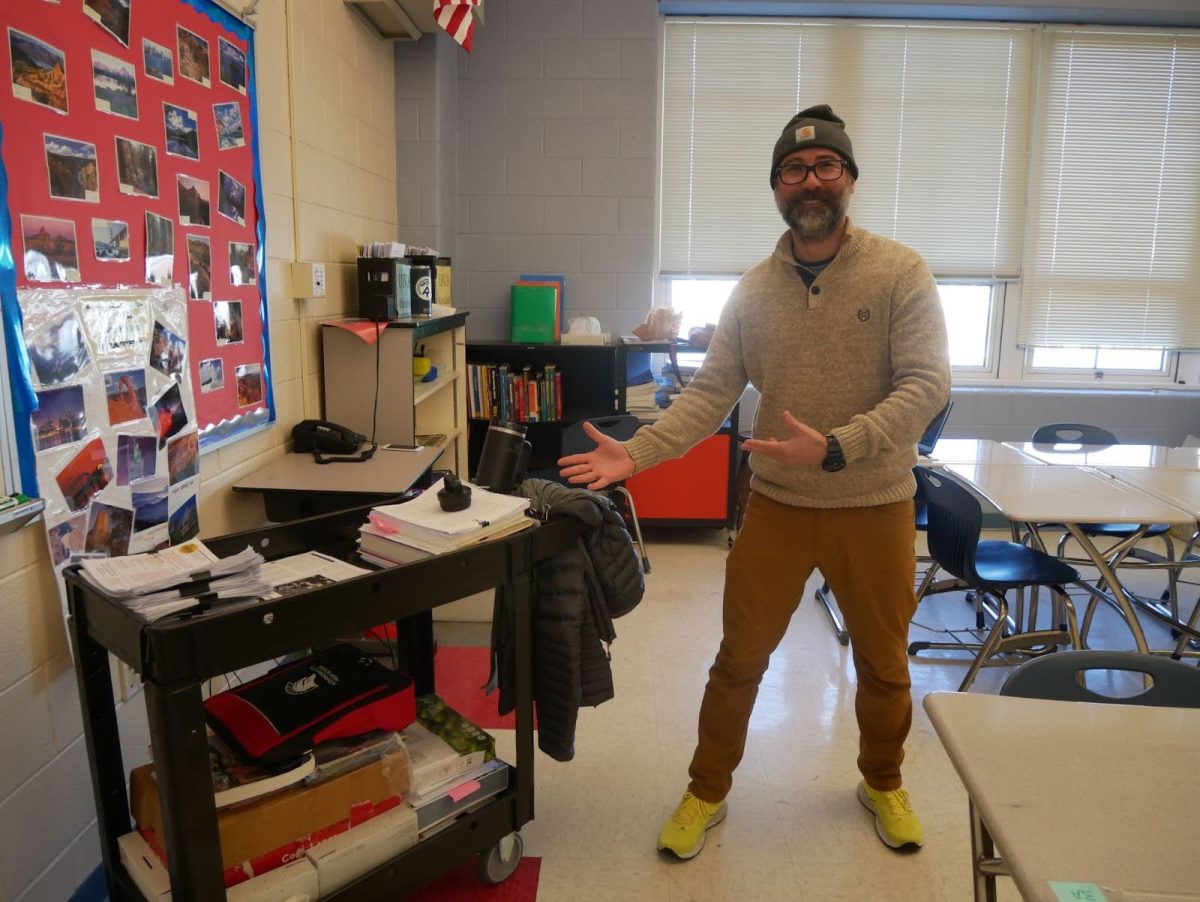 Government and U.S./Virginia History teacher Ryan Beck gestures towards his cart smiling. 
