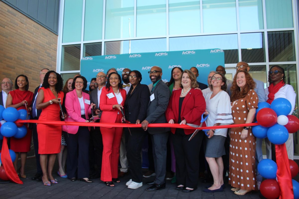 Local leaders cut the ribbon and officially open Minnie Howard. From left: Kirk McPike, city councilmember; Alyia Gaskins, city councilmember; Jim Parajon, city manager; Alicia Hart, ACPS chief operations officer;  Elizabeth Bennett-Parker, Virginia state delegate; Michelle Rief, school board chair;  Canek Aguirre, city councilmember; Justin Wilson, mayor; Melanie Kay-Wyatt, superintendent; John Chapman, city councilmember; junior Zeinab Yassin, student representative to the school board; Alexander Duncan, ACHS executive principal; Jacinta Greene, School Board member; Amy Jackson, vice-mayor; Lance Harrell, Minnie Howard campus administrator; Tim Beaty, school board member; Kelly Booz, school board vice-chair; Ashley Carter Sinclair, King Street campus administrator; Sarah Bagley, city councilmember; Christopher Harris, school board member; Meagan Alderton, school board member.