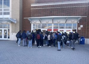 A crowd of roughly 25 students wait outside of the student entrance to the King St. campus.