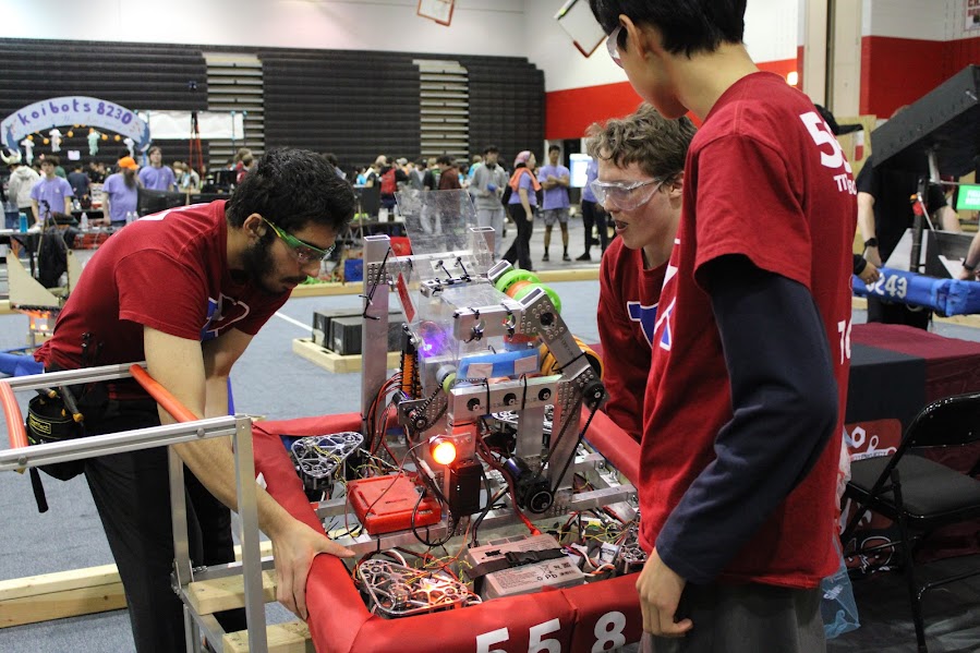 Sophomore Alex Yoon, junior Naematullah Rahmatullah and senior Ricky Ward working together to place the robot onto the playing field. The team’s robot was equipped with red bumpers, signifying their position on the red team, referred to as red alliance.  
