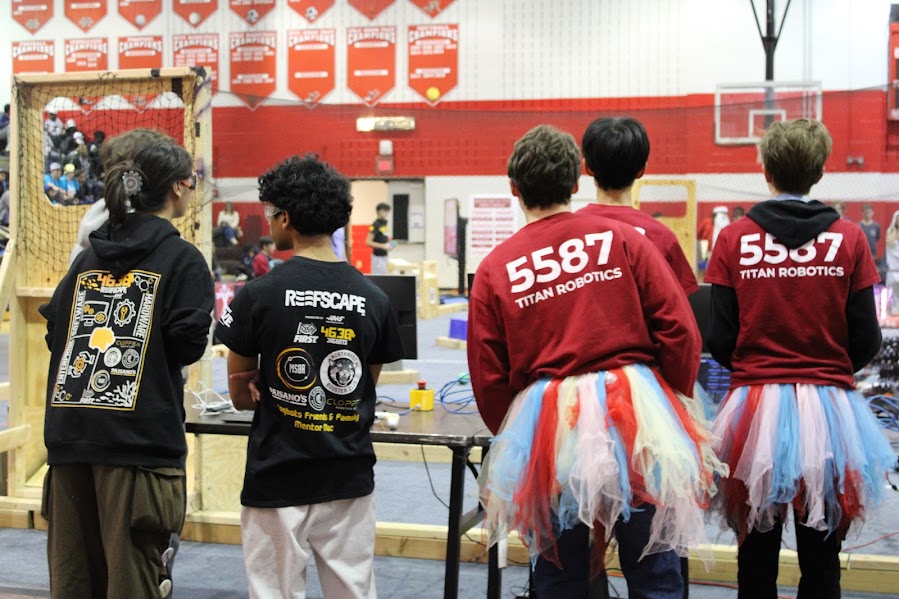Three members of the Titan Robotics team stand next to two members of the Jagbots team. They are in the first 15 seconds of the match, called “auto,” when the drivers are prohibited from controlling the robot and can only rely on what they have already coded the robot to do. 