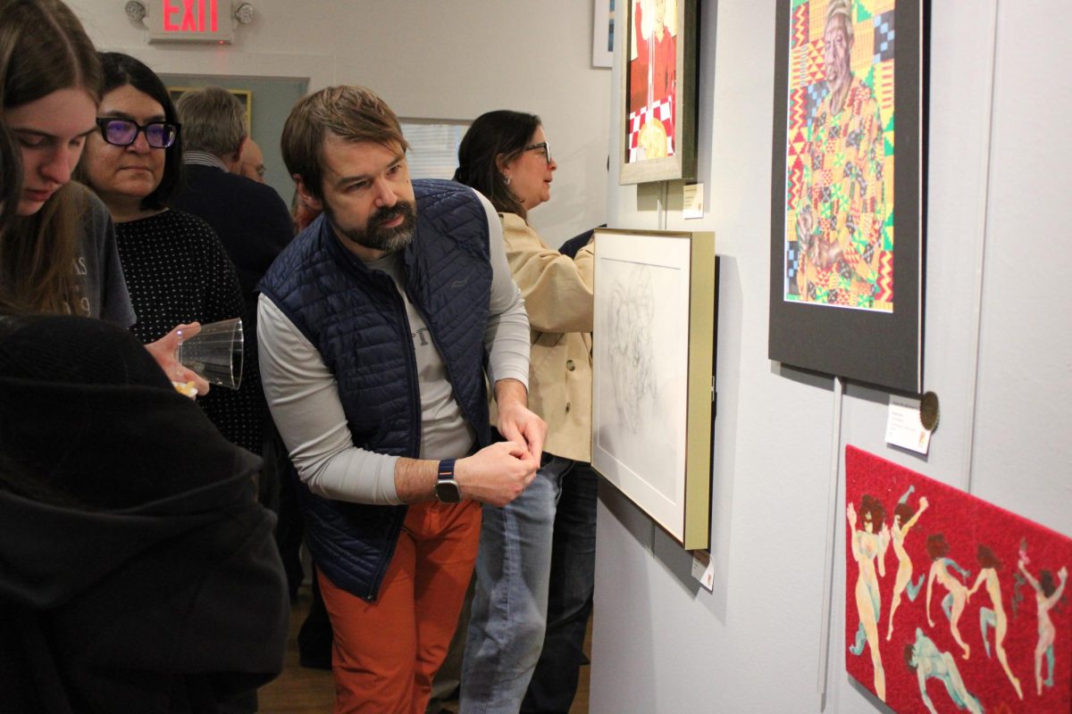 A crowd of people gather to see the award-winning piece by senior Anna McMahon, titled Robed Roots, accompanied by senior Al Ward’s acrylic painting titled Maenads. 
