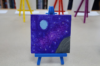 A canvas titled "The Galaxy" featuring stars and planets, painted by Adelaide Sparrow Wilson. Wilson writes, "The U.S.A is beautiful like the galaxy."
